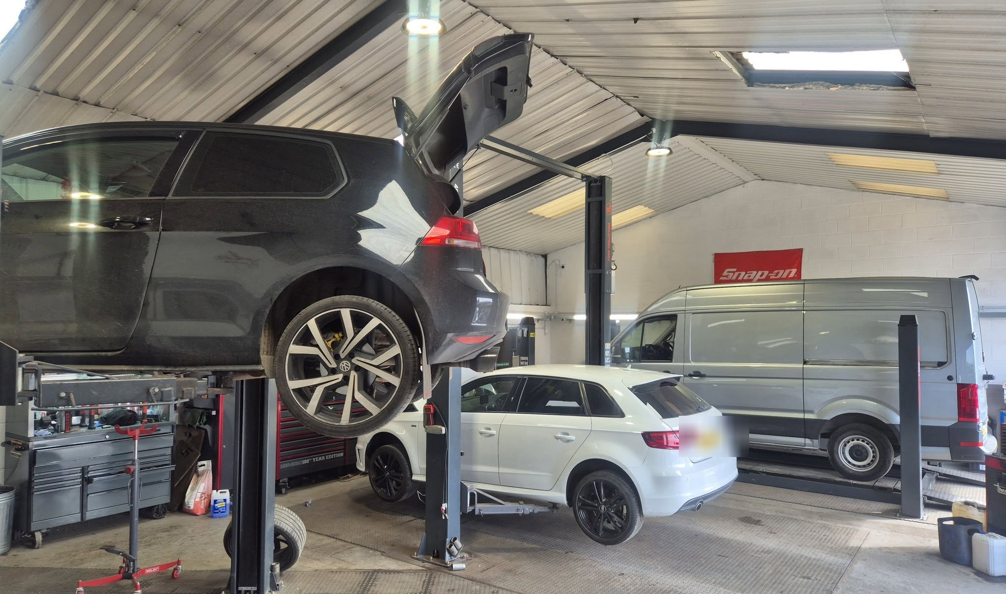 A dark VW estate raised on a two-post lift with a white Audi A3 and a silver van below it in the new workshop
