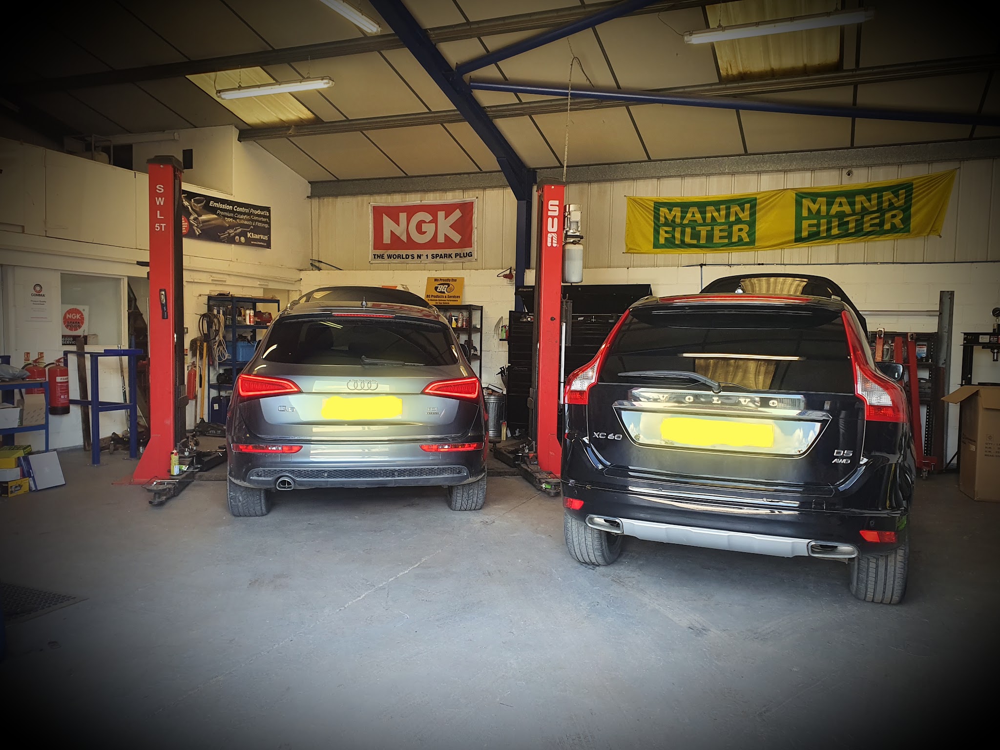 An Audi Q5 and a Volvo XC60 parked on the ramps under NGK and Mann Filter banners